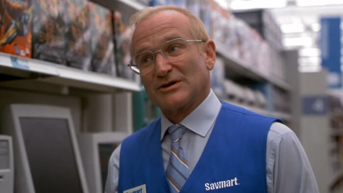 Actor Robin Williams wearing a Savmart vest and glasses, portraying a store employee in a retail setting.