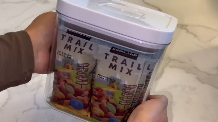 Hands holding a container filled with multiple packs of trail mix, illustrating trends leading to overconsumption. - 27