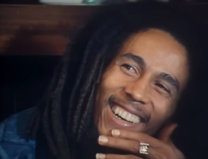 Smiling man with dreadlocks wearing a ring, representing the journey from poverty to super wealthy in a casual setting.