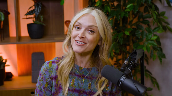 Blonde woman speaking into a microphone in a cozy room, discussing celebrities that many people love but can't stand.