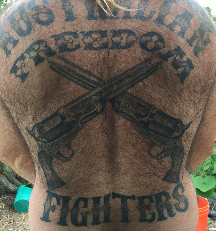 Tattooed back of a vigilante with crossed guns and freedom fighters text symbolizing punishment and justice. - 5