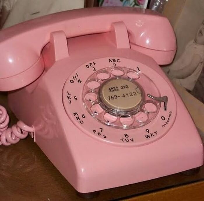 Pink vintage rotary phone on wooden surface, showcasing a classic retro design and numbered dial, vintage things collection