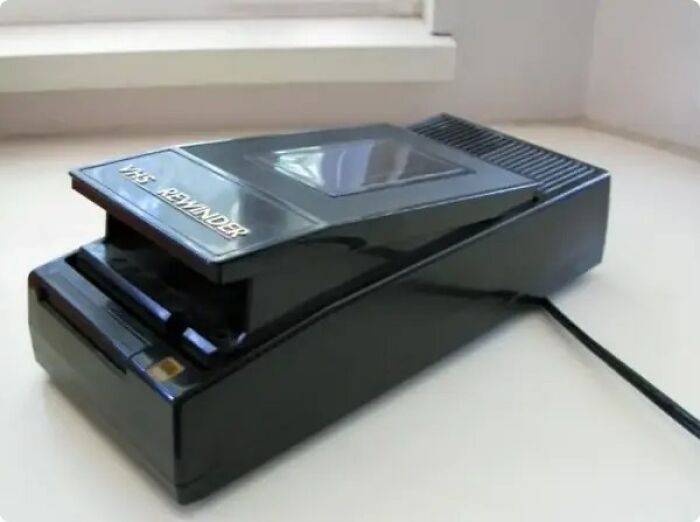 Vintage VHS reminder device in black plastic casing placed on a white surface near a window for nostalgic tech lovers