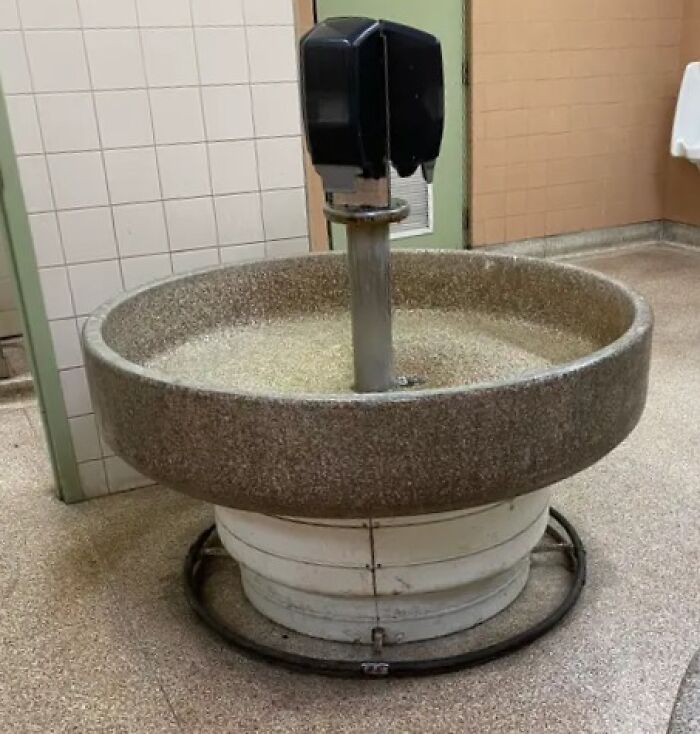 Vintage round stone wash basin with dual soap dispensers mounted on a metal stand in a public restroom.