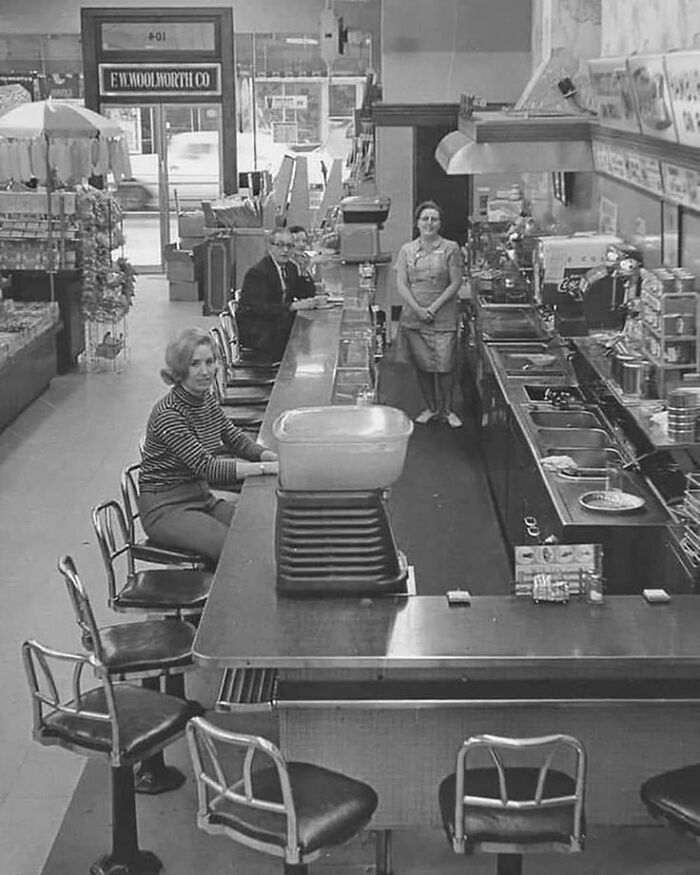 Black and white image of a vintage diner counter with customers seated and waitress standing behind the counter.