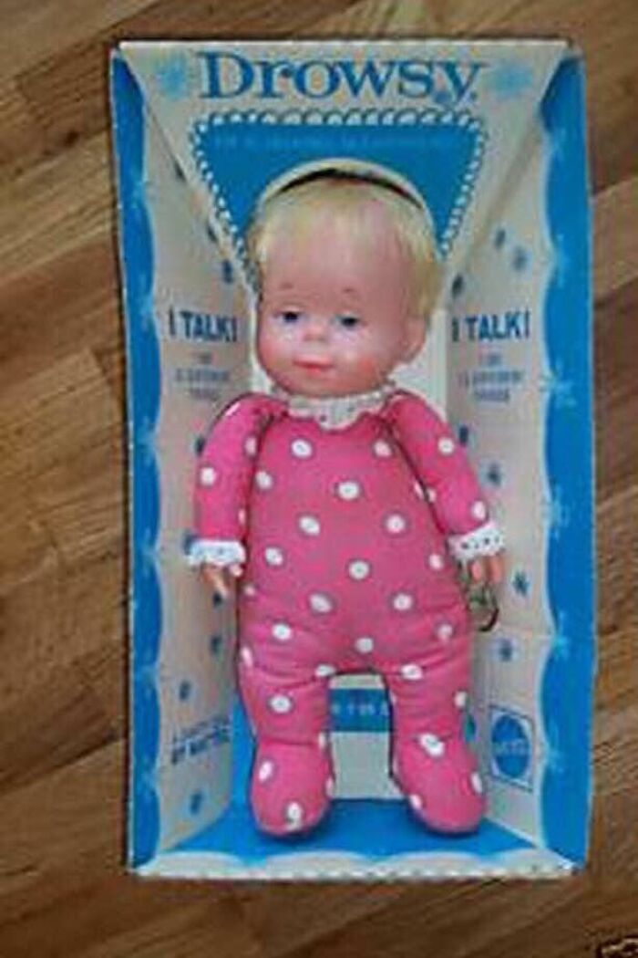 Vintage talking baby doll in pink polka dot pajamas displayed in original retro packaging on wooden floor.