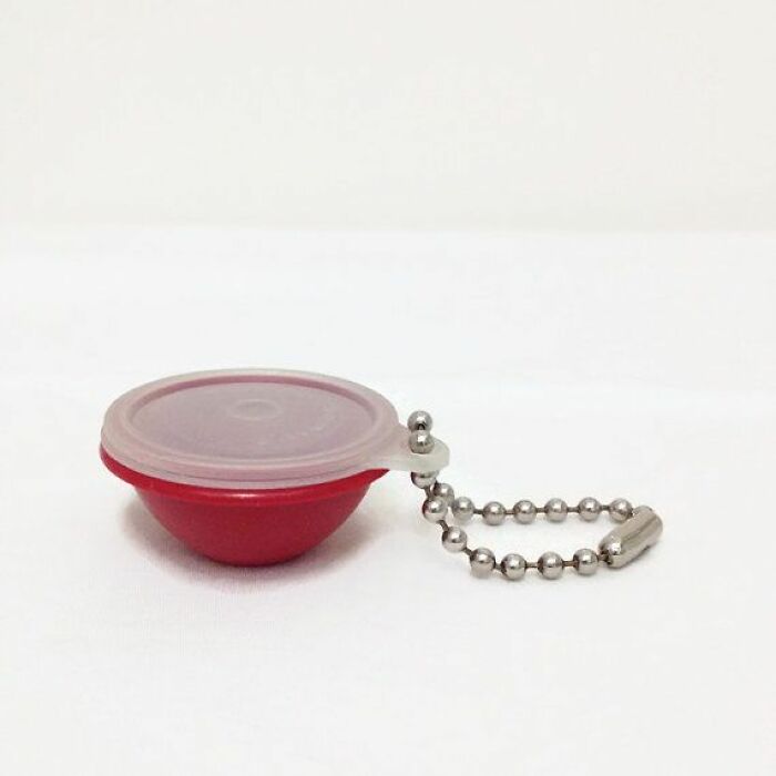 Small vintage red container with a translucent lid and metal ball chain keyring attachment on white background
