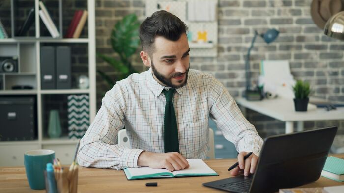 Man in a checkered shirt and green tie working on a laptop and notebook, representing small daily wins from feminists.