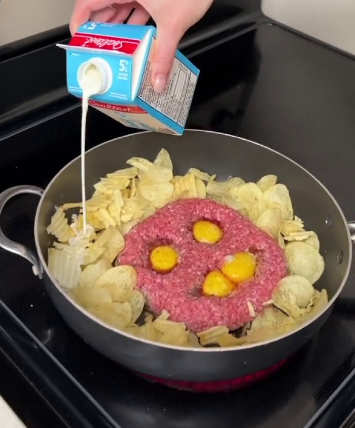 Hand pouring cream into a frying pan with raw ground beef, eggs, and potato chips illustrating overconsumption trends. - 12