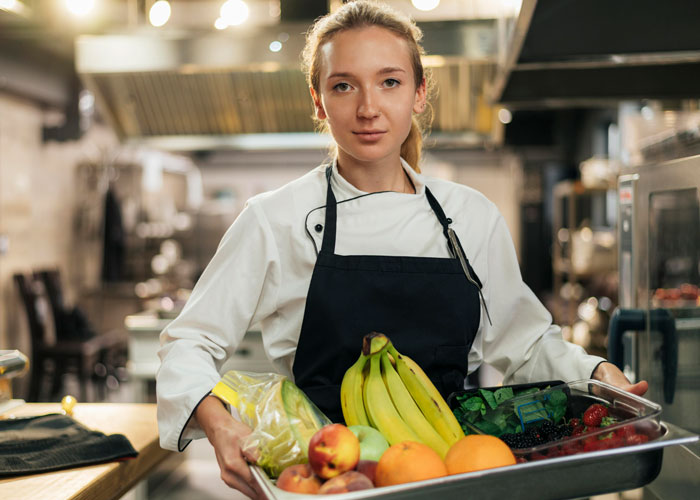 Female caterer holding a tray of fresh fruits in a professional kitchen, relating to bride's protests to change caterer.