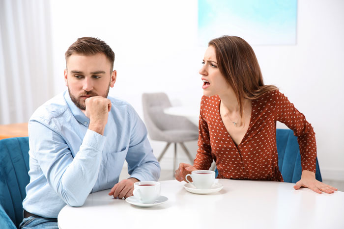 Bride protests to change caterer while groom looks upset during a tense wedding planning discussion at home.
