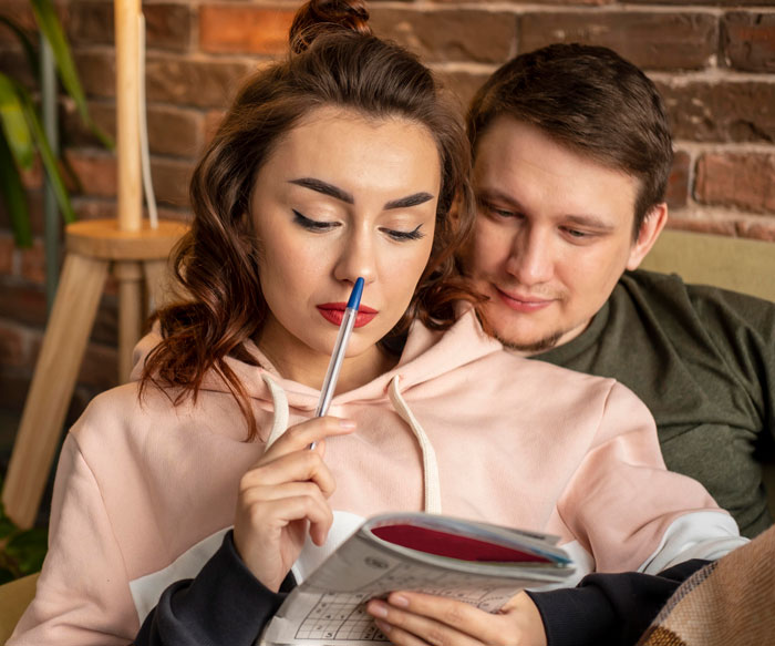 Bride thoughtfully holding pen while reading, with groom sitting close, illustrating bride's protests over wedding caterer choice.