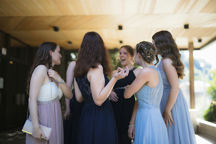 Group of women dressed for a wedding, one wearing a white dress similar to a bride's gown in a sunny outdoor setting. - 11