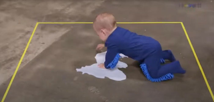Baby crawling on a floor wearing mop slippers, one of the weird inventions designed for cleaning while moving.