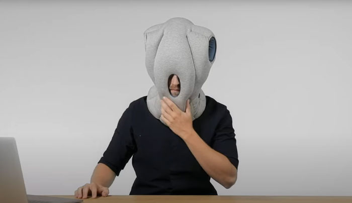 Person wearing a weird invention headgear designed for comfort and privacy while working at a desk with a laptop nearby.