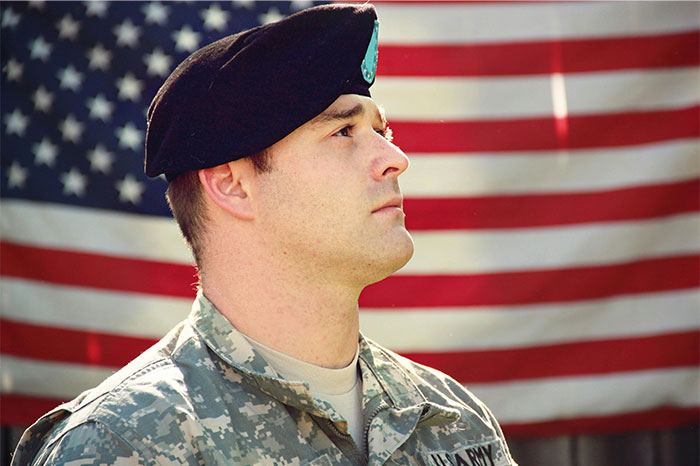 US soldier in uniform standing in front of American flag, illustrating things non-Americans find weird about the US. - 14