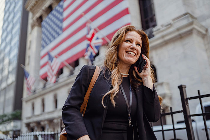 Smiling woman talking on phone outside a building with American flags, illustrating things non-Americans find weird about the US - 31