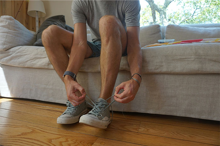 Person sitting on a couch tying sneaker laces indoors, illustrating everyday US habits non-Americans find weird. - 38