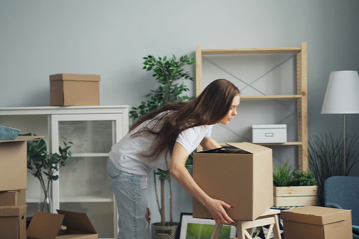 Young woman unpacking boxes in a room, illustrating everyday normal life in the US seen as weird by non-Americans. - 32