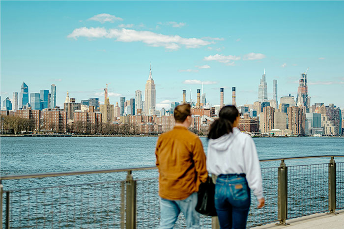 Two people walking by the river with a city skyline in the background, showcasing US cultural scenes seen as normal. - 13