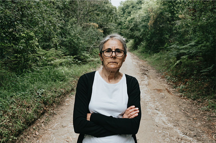 Older woman with glasses standing on a forest path, representing things non-Americans find weird about the US - 17