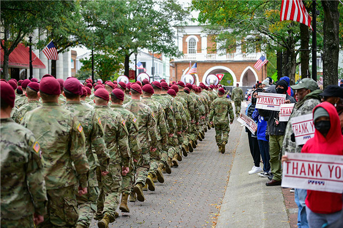US soldiers marching in uniform with civilians holding thank you signs in a patriotic scene considered normal by locals. - 9