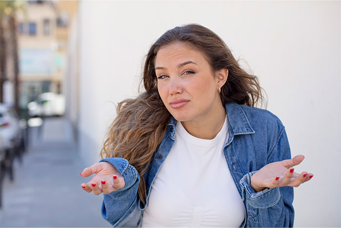 Young woman in a denim jacket shrugging outdoors, illustrating things non-Americans find weird about the US. - 18