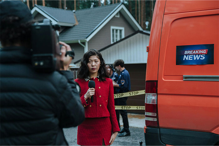Female reporter in a red suit filming breaking news near police tape and an orange news van, illustrating US weird local customs. - 33