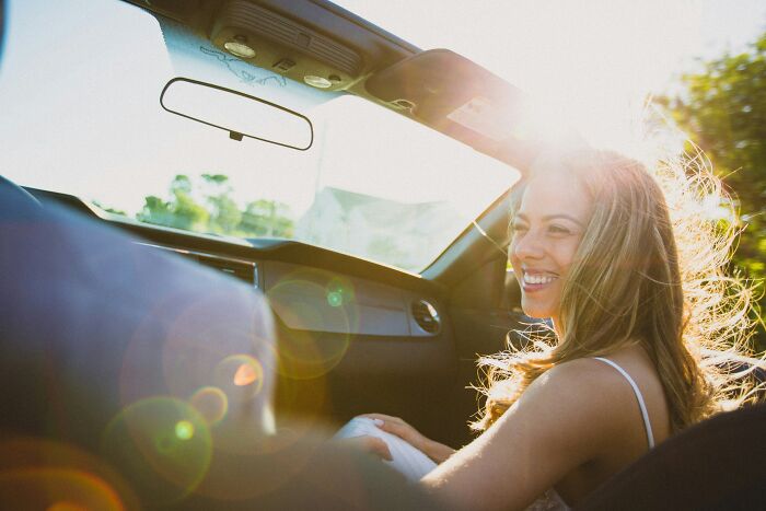 Smiling woman passenger enjoying a sunny car ride while truckers share craziest things seen on the road. - 11