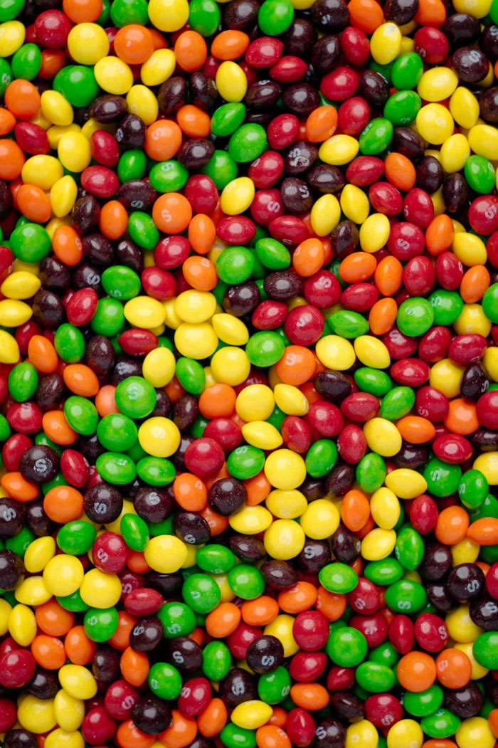 Colorful American Skittles candy pieces scattered closely together, representing American foods banned in other countries.