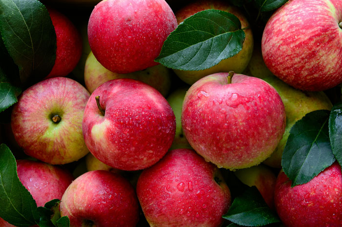 Close-up of fresh red apples with green leaves, illustrating American foods banned in other countries and reasons why.