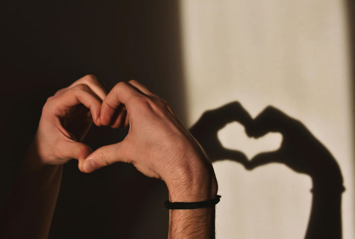Hands forming a heart shape with shadow on wall, symbolizing psychological clues hidden in dreams about people.