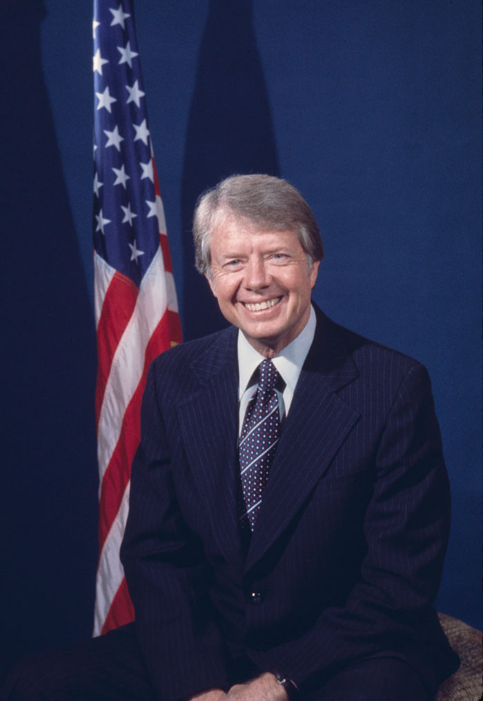 Former US president Jimmy Carter sitting with American flag in background representing highest IQ presidents ranking.