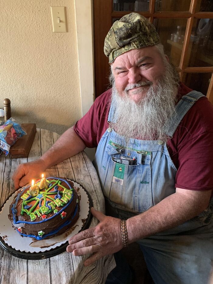 Smiling man in overalls celebrating birthday with a chocolate cake, reflecting wholesome people that make the world better.