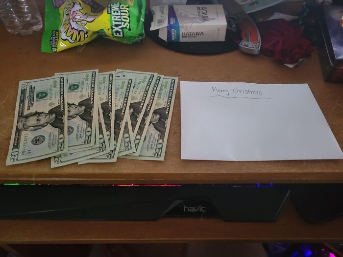 Twenty-dollar bills spread on a desk next to an envelope with Merry Christmas written, showcasing wholesome people kindness.