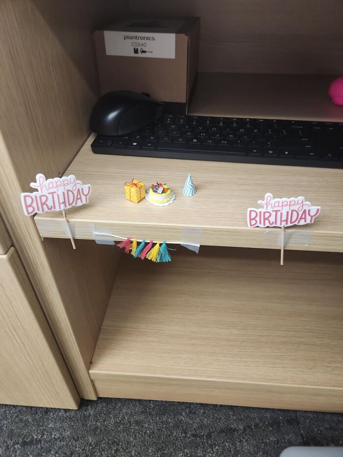 Tiny birthday decorations arranged on an office desk shelf, showcasing wholesome moments with people and animals.