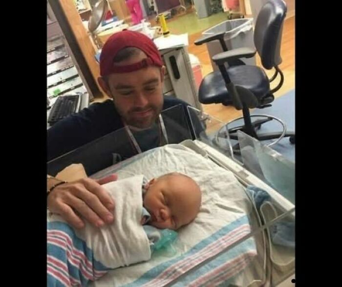 Man wearing red cap gently touching sleeping newborn in hospital nursery, showcasing wholesome and amazing moments.