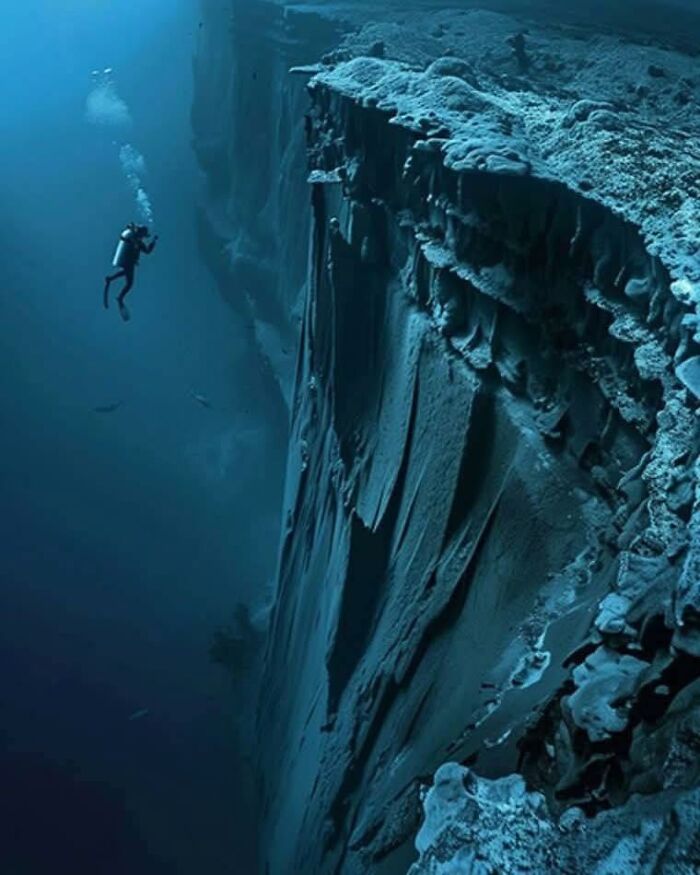 Scuba diver exploring a deep underwater cliff in the wonderful world of ocean depths and marine life.