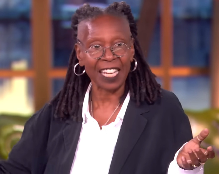 Whoopi Goldberg wearing glasses and blazer, speaking on a talk show about CEO Andy Byron and Coldplay kiss cam incident.