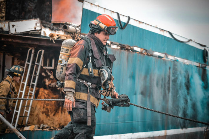 Firefighter in protective gear near a rusted ship, illustrating the wife’s fear her husband is lost at sea. Firefighter in protective gear near a rusted ship, illustrating the wife’s fear her husband is lost at sea.