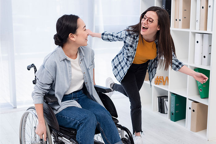 Woman in wheelchair smiling at friend in casual clothes, highlighting themes of caring for disabled siblings and family challenges.