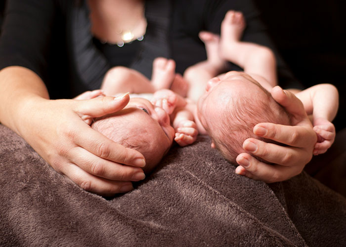 Hands gently cradling newborn twins on a soft blanket, illustrating the reality of parenting twins and solo trip challenges. - 10