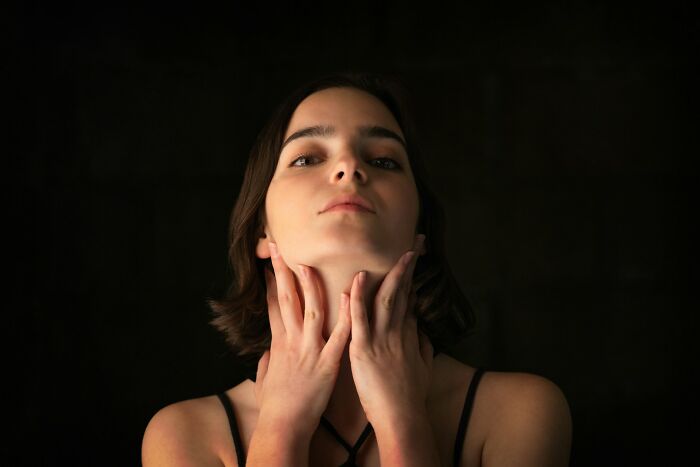 Young woman with short hair touching her neck, highlighting mysterious body quirks in a dark, moody setting.