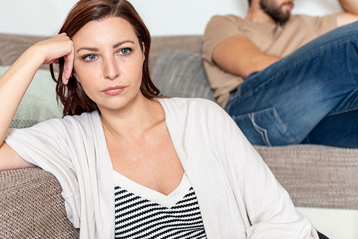 Woman looking frustrated on a couch while her partner sits in the background, highlighting in-laws demand and clapback conflict. - 5
