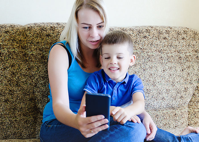 Mother and young son sitting on a couch looking at a smartphone, illustrating co-parenting and family interaction challenges.