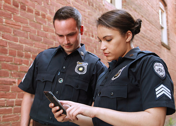Two police officers in uniform checking a phone, illustrating CPS involvement in co-parenting misunderstanding cases.