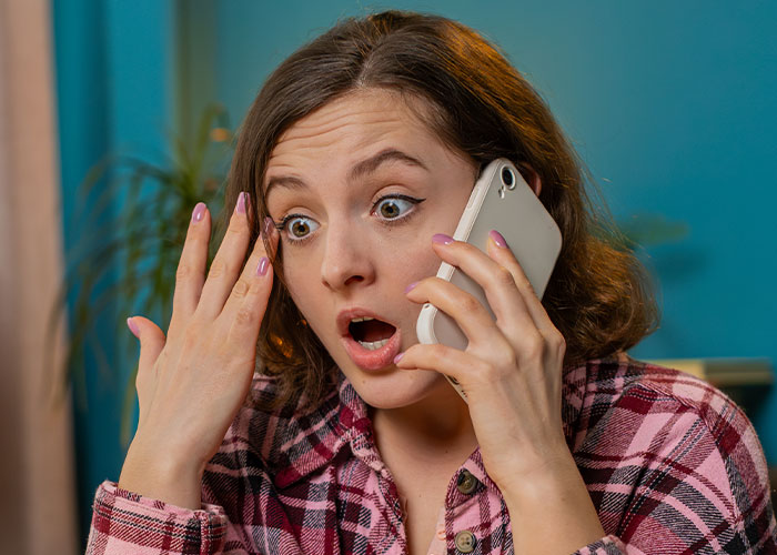 Woman in plaid shirt looking shocked while on a phone call, depicting co-parenting misunderstanding and CPS involvement.