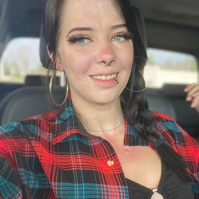 Woman burned in gas station explosion with visible scars, smiling confidently and wearing a red plaid shirt inside a car. - 7