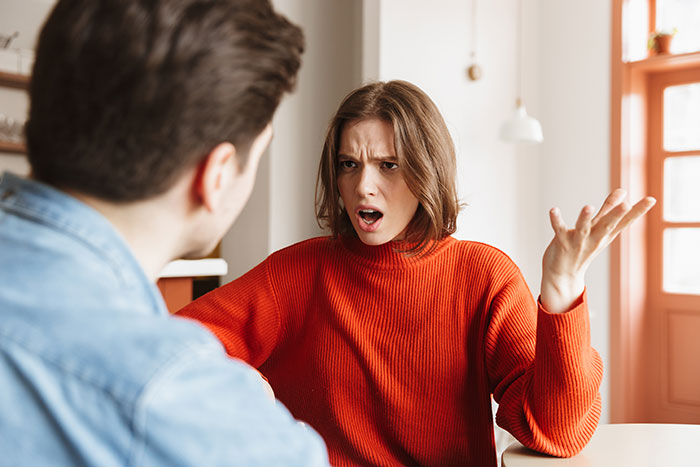 Woman in an orange sweater looking upset and confused while talking to man about fiancee mad over MIL having house key. - 6