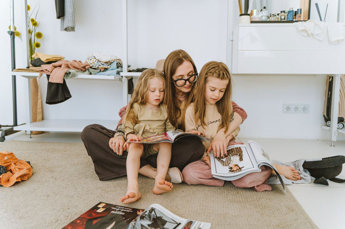 Woman sitting on floor reading magazines with two young girls, reflecting on cutting off friend in abusive marriage.